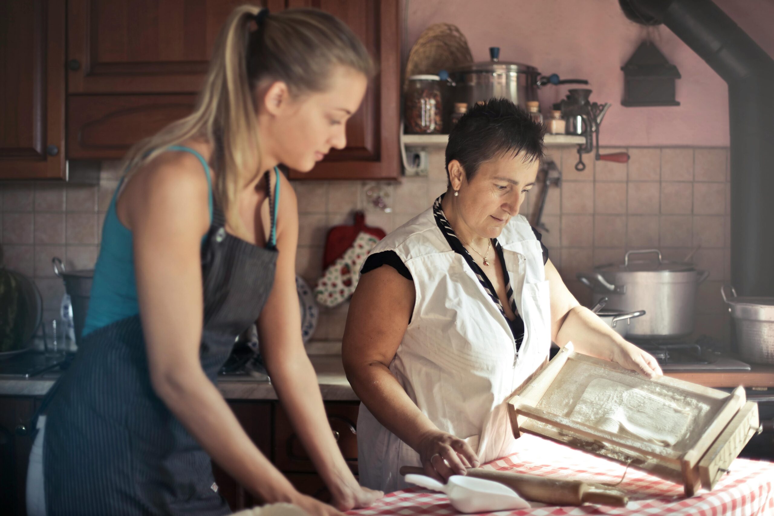  Dos mujeres en una cocina, una mayor y otra más joven, trabajan juntas en la preparación de alimentos, demostrando el proceso de enseñanza práctica y colaboración.